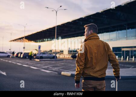 Giovane uomo con i bagagli per raggiungere a piedi i terminal dell'aeroporto a sunrise. Foto Stock