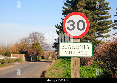 A 30 mph segno e nome del villaggio del Langham Road entrando nel North Norfolk villaggio di Blakeney, Norfolk, Inghilterra, Regno Unito, Europa. Foto Stock