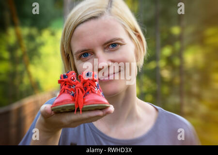 Ragazza con bellissimi occhi azzurri tenendo in mano un piccolo rosso scarpe per bambini Foto Stock