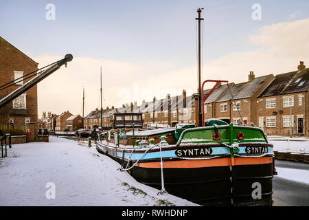 Vintage chiatte ormeggiate lungo la congelati beck (canale) e coperta di neve fiancheggiate da case in Beverley, Yorkshire, Regno Unito. Foto Stock