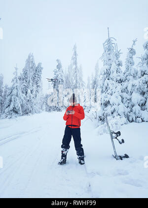 Snowboarder controlla il fuco durante una pausa nella pratica del pattinaggio. Incantevole paesaggio invernale sullo sfondo Foto Stock