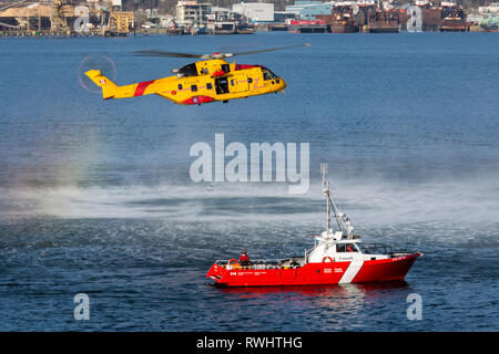 Un Royal Canadian Air Force CH-148 Cormorant elicottero vola al di sopra di un settore della pesca e degli oceani del Canada barca durante un esercizio di formazione nel porto di Vancouver, British Columbia, Canada. Foto Stock