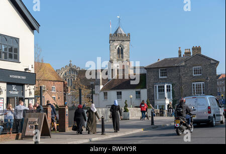 Salisbury, Wiltshire, Inghilterra, Regno Unito. Febbraio 2019. Donna musulmana in lunghi abiti neri e sfondo della chiesa di San Tommaso. Foto Stock