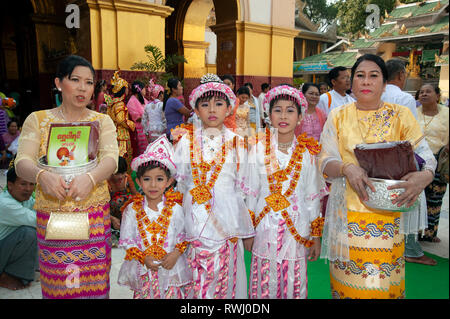 Orgogliosi di birmani famiglia con la loro luminosa in costume trucco pesantemente i ragazzi che frequentano i loro prossimi di età cerimonia in Myanmar Mandalay Foto Stock