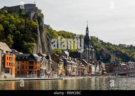 Città di Dinant lungo il Fiume Mosa con una grande chiesa steeple e alte scogliere con una fortezza di pietra sulla sommità; Dinant, Belgio Foto Stock