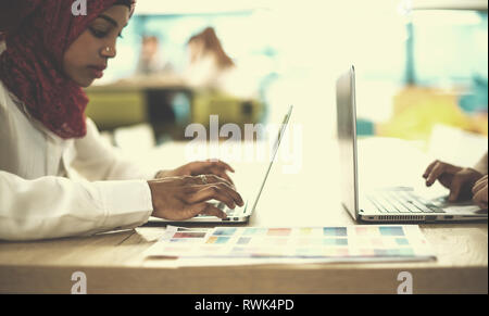 Giovane e moderno musulmano nero business donna che indossa un rosso hijab,lavorando sul computer portatile in ufficio di avvio. La diversità, multirazziale concept Foto Stock