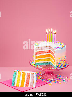 Colorato rainbow torta di compleanno con candele su un sfondo rosa. Foto Stock