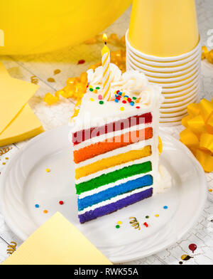 Fetta di colorati torta di compleanno con illuminata candela di compleanno e partito di colore giallo con decorazioni in background Foto Stock