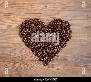 Vista aerea di chicchi di caffè disposti in una forma di cuore su di un legno marrone dello sfondo. Mi piace il caffè. Foto Stock