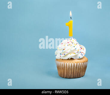 Un compleanno Cup cake con glassa di crema di burro, spruzza e un numero accesa una candela di compleanno. Foto Stock