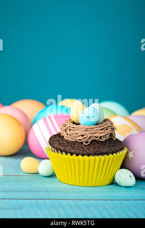 Colorate le uova di Pasqua e tortina con nido su uno sfondo blu. Foto Stock