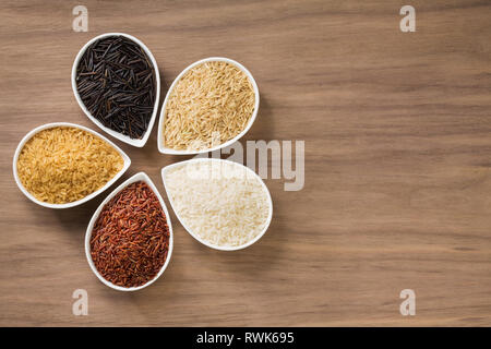 Una colorata varietà di riso in ciotole su uno sfondo di legno Foto Stock