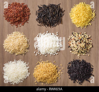 Pile di differenti varietà di riso su un sfondo di legno compreso il gelsomino, basmati, riso selvatico, risotto e scottati in rosso, bianco, marrone e nero Foto Stock