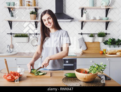 Felice ragazza giovane prepara il cibo sano in cucina per affettare cetrioli Foto Stock