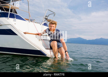 Giovane uomo appoggiata dalla barca a vela sul lago Chiemsee, ritratto, Baviera, Germania Foto Stock