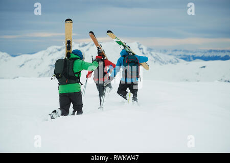 Paesaggio con tre sciatori maschio trascinarsi faticosamente verso la montagna, vista posteriore, Alpe-d'Huez, Rhone-Alpes, Francia Foto Stock