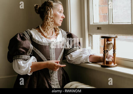 Ritratto di una giovane e bella donna in ornato abito storico- i suoi vestiti sono belle, sta in piedi da una porta nel profondo del pensiero e sembra triste. Foto Stock