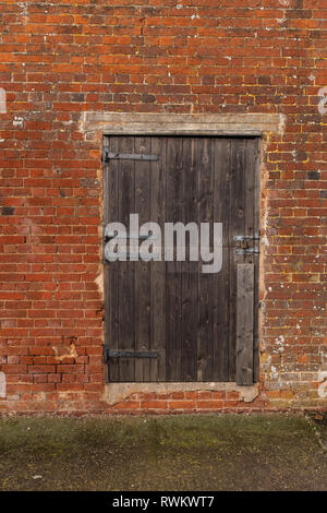 Una chiusura di un di legno stagionato fienile porta in un muro di mattoni di un edificio in un agriturismo Foto Stock