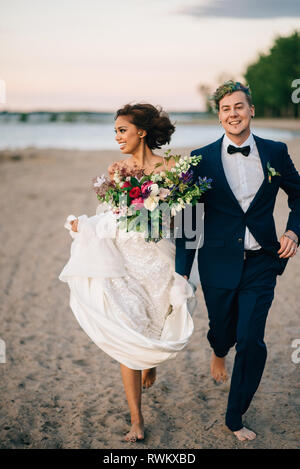 Sposa e lo sposo correre a piedi nudi sul lago, lago Ontario, Toronto, Canada Foto Stock