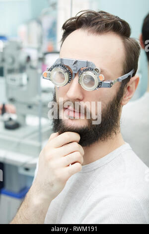 Giovane uomo con telai di prova in Oftalmologia Clinica Foto Stock