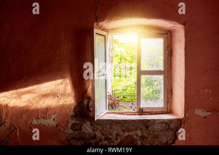 Interno di una rovina il vecchio cottage con una luce rosa di parete e la rottura di una finestra in legno telaio guardando attraverso un rurale prato verde paesaggio del campo Foto Stock