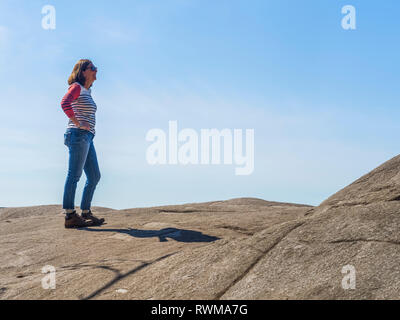 Una donna si erge a Cava sulla roccia Baden-Powell Trail contro un cielo blu, Deep Cove, North Vancouver; Vancouver, British Columbia, Canada Foto Stock