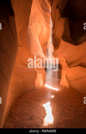 Flussi di luce solare attraverso un foro naturale in pietra arenaria alla sabbia al di sotto, Superiore Antelope Canyon; Arizona, Stati Uniti d'America Foto Stock