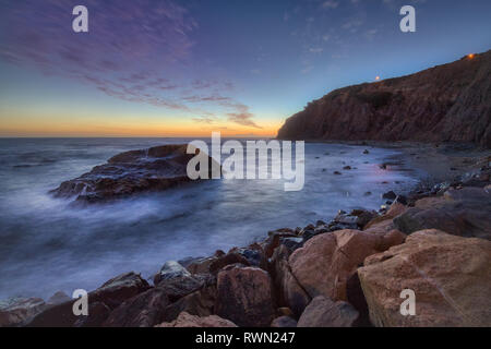 Una lunga esposizione foto di coniatura alte scogliere e le onde si infrangono in un grande rock formazione dopo il tramonto, Dana Point, California Foto Stock