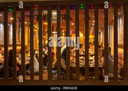 Vista attraverso il vetro a doghe in un ristorante asiatico con ristoranti per famiglie. Foto Stock