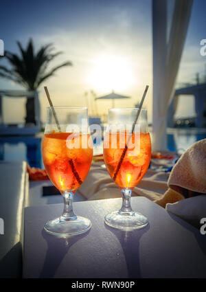 Due bicchieri con Aperol Spritz (aperitivo cocktail costituito da Prosecco, Aperol Soda e acqua) vicino a una piscina al tramonto Foto Stock
