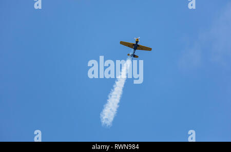 Aeroplano non identificabili esecuzione di volo acrobatico sul cielo blu. Traccia di fumo dietro. Arresto del motore Foto Stock