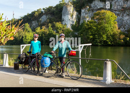 Maschi e femmine di ciclista permanente sulla pista ciclabile lungo una ringhiera di banca di fiume con scogliere in background e cielo blu, a sud di Namur, Belgio Foto Stock