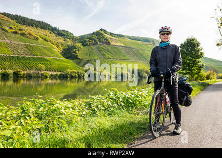 Ciclista femmina lungo il fiume percorso in bicicletta con ripidi vigneti sui versanti del fiume in background, vicino Piesport; Germania Foto Stock