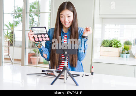 Bella asiatica influencer donna la registrazione compongono tutorial utilizzando la fotocamera dello smartphone urlando orgoglioso e celebrando la vittoria e il successo molto eccitato, Foto Stock