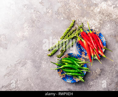 Peperoni di vari tipi di rosso verde nero in una ciotola con ornamenti colorati su sfondo grigio. Schema piatto. Copia dello spazio. Vista da sopra. Foto Stock