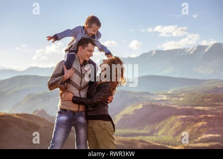 La famiglia felice con il giovane figlio si erge contro le montagne Foto Stock