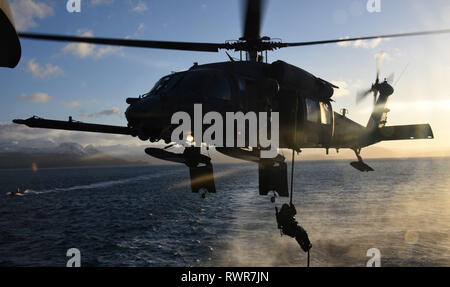 Un 176ala, 210th Rescue Squadron Alaska Air National Guard UH-60G Pave Hawk elicottero equipaggio libra mentre un membro della Guardia Costiera della sicurezza marittima la risposta del team di West fast-corde per il guardacoste Alex Haley (WMEC 39) ponte di volo in una formazione congiunta esercizio nei pressi di Kodiak, Alaska, Feb 23, 2019. I membri del team praticata fast roping evoluzioni, scaletta salite e una serie di esercizi a bordo della nave a rimanere tecnicamente competente in tecniche avanzate necessarie per la protezione della nazione da minacce sia in mare e in aria. Stati Uniti Coast Guard foto di Sottufficiali di terza classe Lauren de Foto Stock