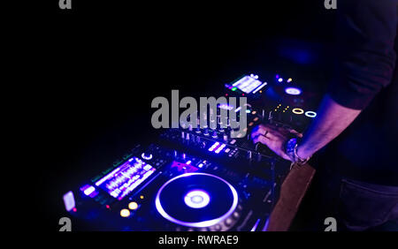 Morbida vista di man mano disc jockey di miscelazione e miscelazione di brani musicali sul suo ponte nelle tenebre di una parte o di un night club.Copia spazio per il testo. Foto Stock