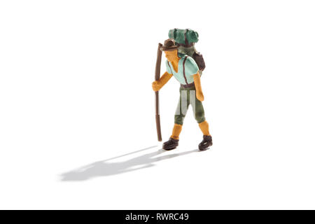 Maschio in miniatura backpacker con zaino trekking sulle montagne con le sue scarpe da trekking e bastone isolato su bianco con ombra e spazio di copia Foto Stock