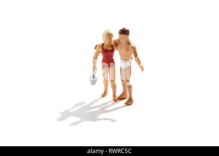 Amorevole coppia in miniatura in piedi sotto braccio su una spiaggia nella suite di balneazione portante una benna isolato su bianco con ombra Foto Stock