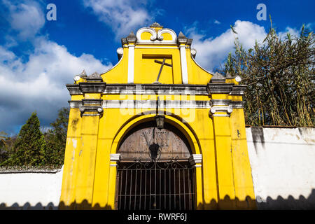 Cappella giallo facciata della chiesa con la croce storta sotto la nuvola blu cielo, Antigua, Guatemala Foto Stock