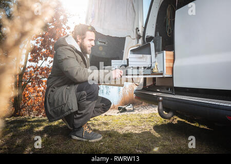 Uomo di fronte a un van utilizzando una build in fornello da campeggio Foto Stock