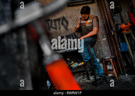 Un colombiano meccanico che lavora su un motore in una riparazione auto shop in Barrio triste, Medellín, in Colombia. Foto Stock