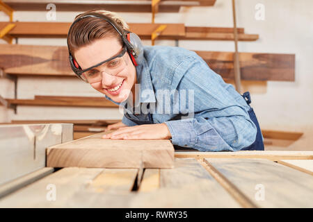 Giovane donna come falegname partecipante lavora con il legno su una sega circolare in falegnameria Foto Stock