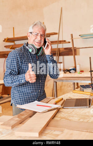 Senior artigiano mantiene il suo pollice in su mentre si parla al telefono cellulare Foto Stock