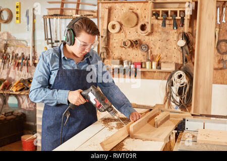 La donna come un falegname apprendista lavora con un trapano in officina Foto Stock