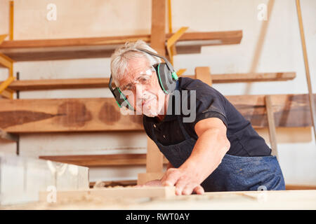 Senior uomo come carpentiere seghe di legno in falegnameria o lavori di falegnameria officina Foto Stock