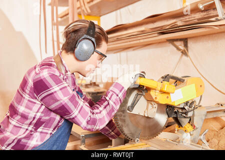 Giovane donna come un carpentiere o falegname apprendista lavora con il legno in corrispondenza della troncatrice Foto Stock