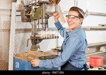 Donna felice come un falegname apprendista lavora sul trapano in officina Foto Stock