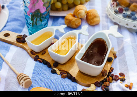 Set di tre sauceboats bianco con il dolce miele sul vassoio in legno a picnic food lay out dello sfondo. Foto Stock